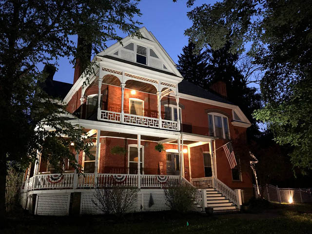 Hatch House Bed and Breakfast, an old fashioned brick building with white porches, lit up at twilight