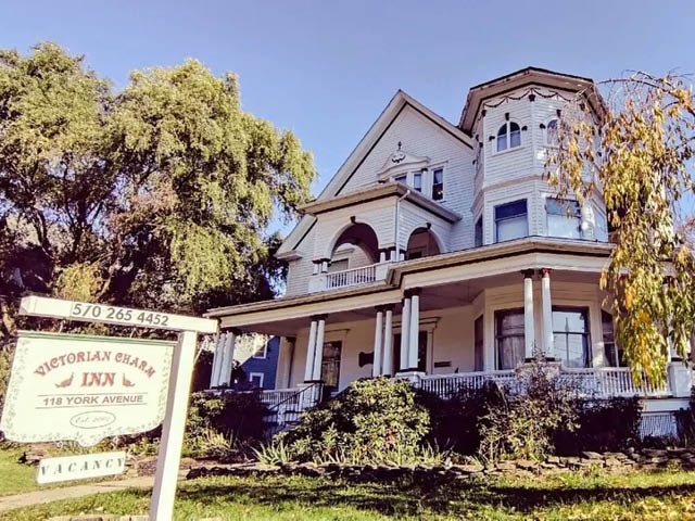 View of the facade of Victorian Charm Inn, a white Victorian mansion, set among trees