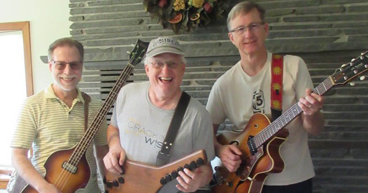 Three band members of the Flat Wounds posing and smiling with their instruments.